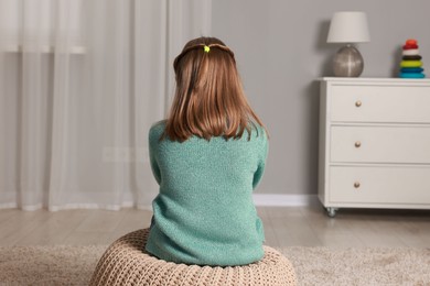 Autism concept. Lonely little girl on pouf at home, back view