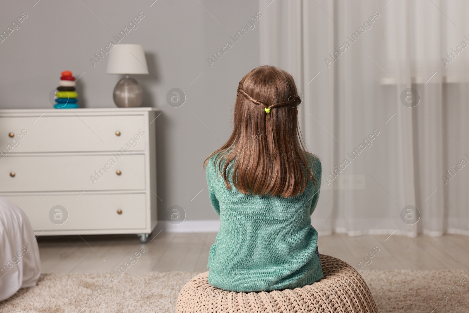 Photo of Autism concept. Lonely little girl on pouf at home, back view