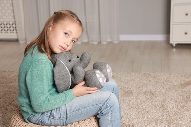 Photo of Autism concept. Lonely little girl with toy bunny on pouf at home, space for text