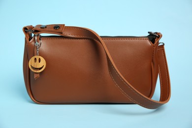 Photo of Bag with wooden keychain in shape of smiley face on light blue background