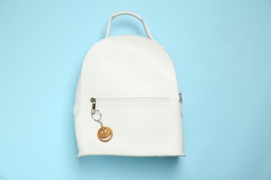 Photo of Backpack with wooden keychain in shape of smiley face on light blue background, top view