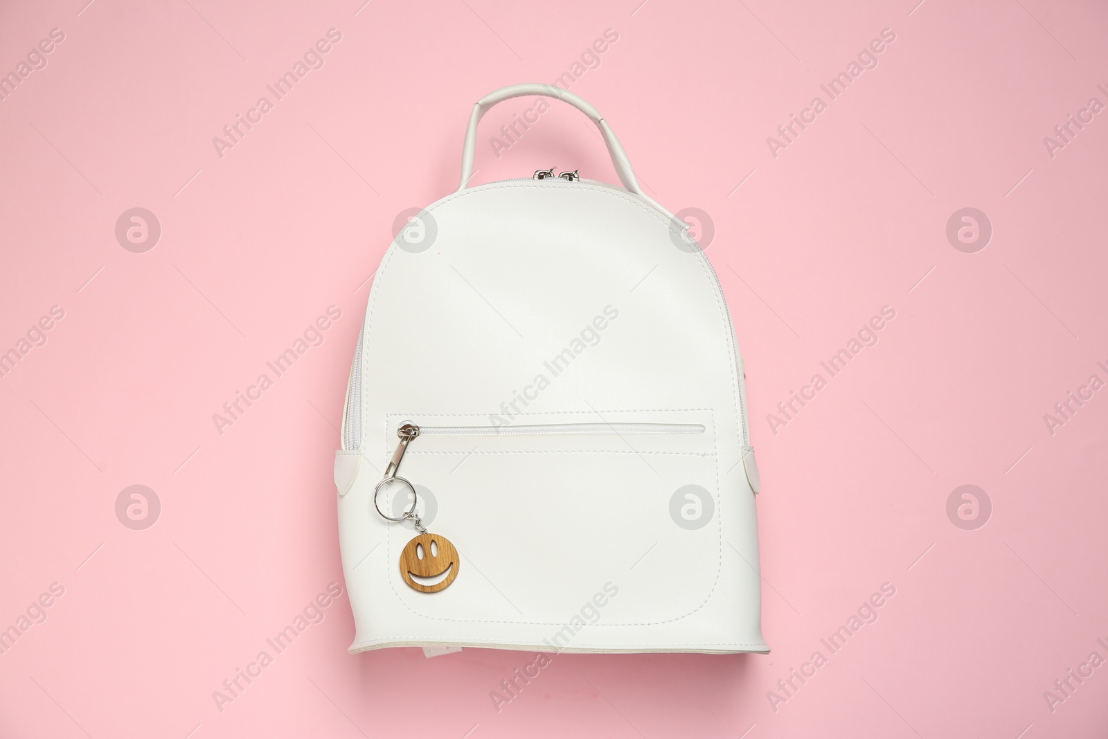 Photo of Backpack with wooden keychain in shape of smiley face on pink background, top view