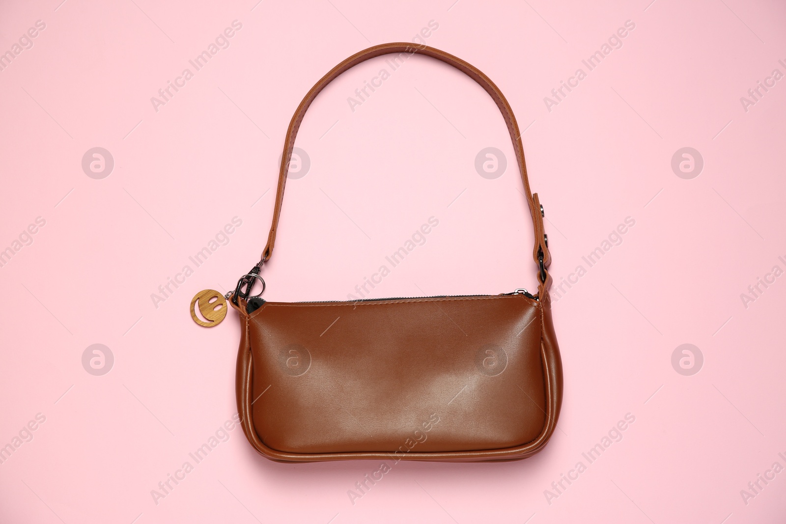 Photo of Brown bag with wooden keychain in shape of smiley face on pink background, top view