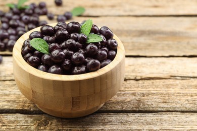 Photo of Ripe acai berries and leaves in bowl on wooden table, closeup. Space for text