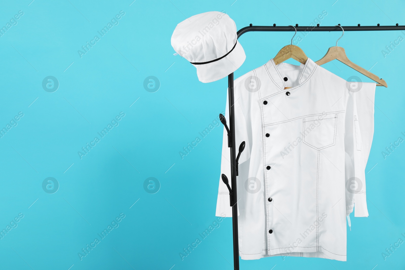 Photo of Chef's uniform on clothing rack against light blue background, space for text