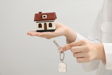 Photo of Woman holding key with keychain and house model on light grey background, closeup