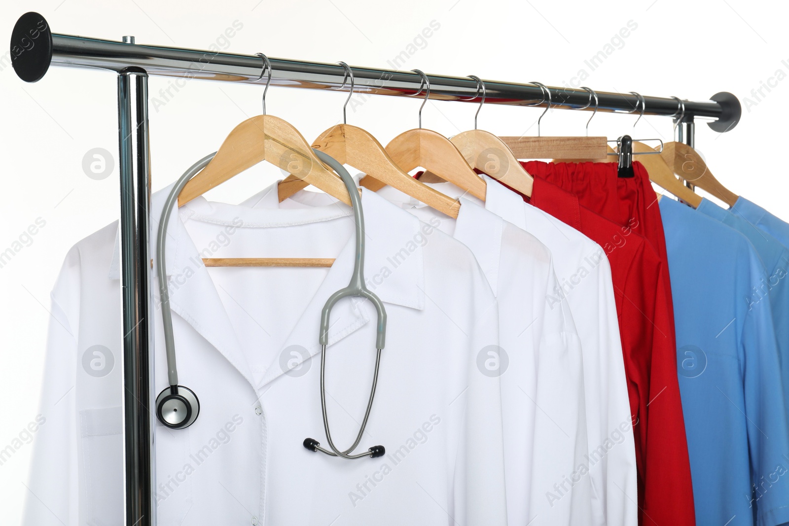 Photo of Different medical workers' uniforms and stethoscope on clothing rack against white background