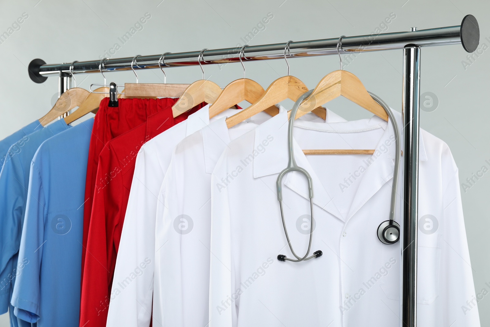 Photo of Different medical workers' uniforms and stethoscope on clothing rack against white background