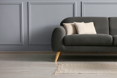 Stylish sofa with cushions near grey wall, space for text