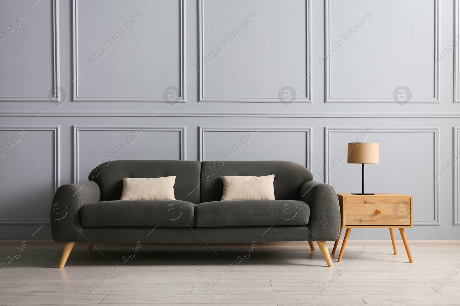 Photo of Stylish sofa with cushions and lamp on side table near grey wall