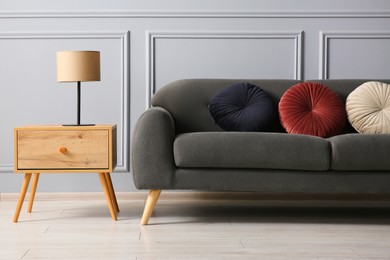 Stylish sofa with cushions and lamp on side table near grey wall