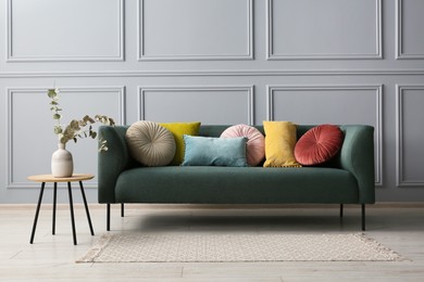 Stylish sofa with cushions and eucalyptus branches in vase on side table near grey wall