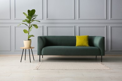 Photo of Stylish sofa with cushion and green plant near on side table grey wall