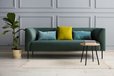 Photo of Stylish sofa with cushions, green plant and books on side table in room