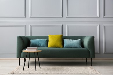 Stylish sofa with cushions and books on coffee table in room