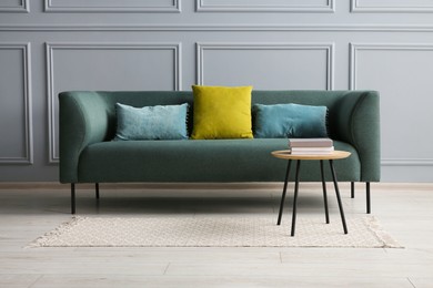 Stylish sofa with cushions and books on coffee table in room