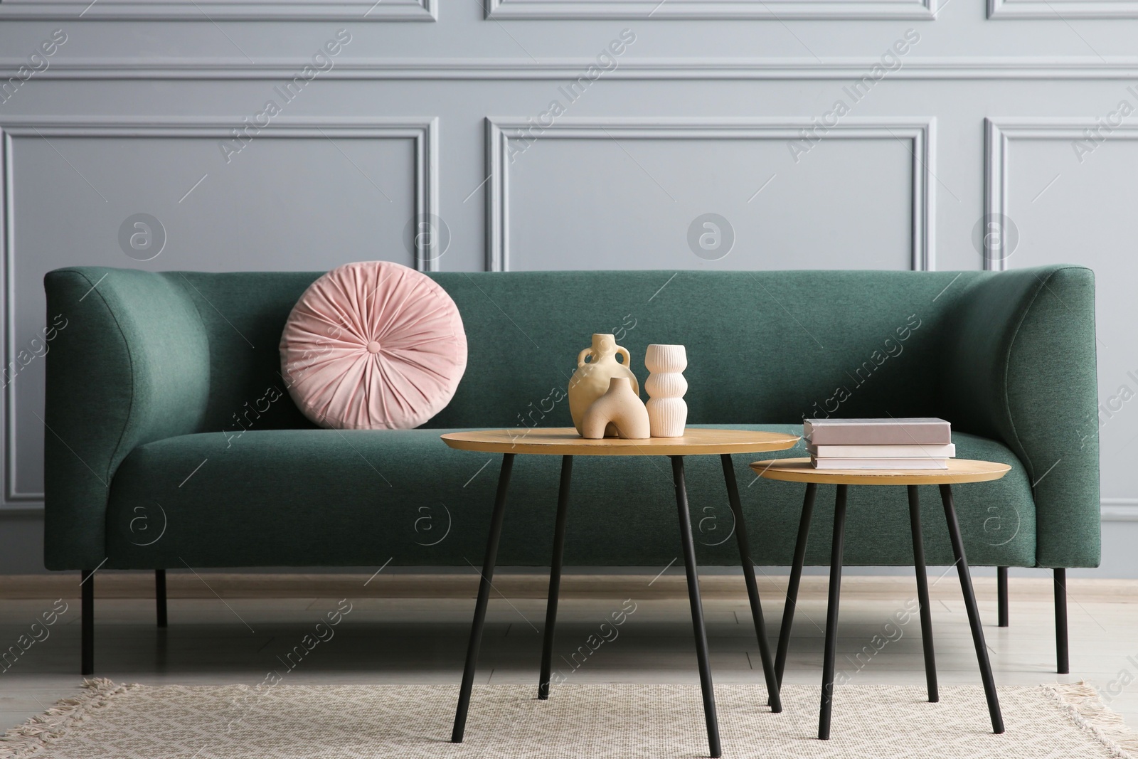 Photo of Stylish sofa with cushion, books and decor elements on nesting tables in room