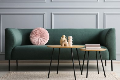 Stylish sofa with cushion, books and decor elements on nesting tables in room