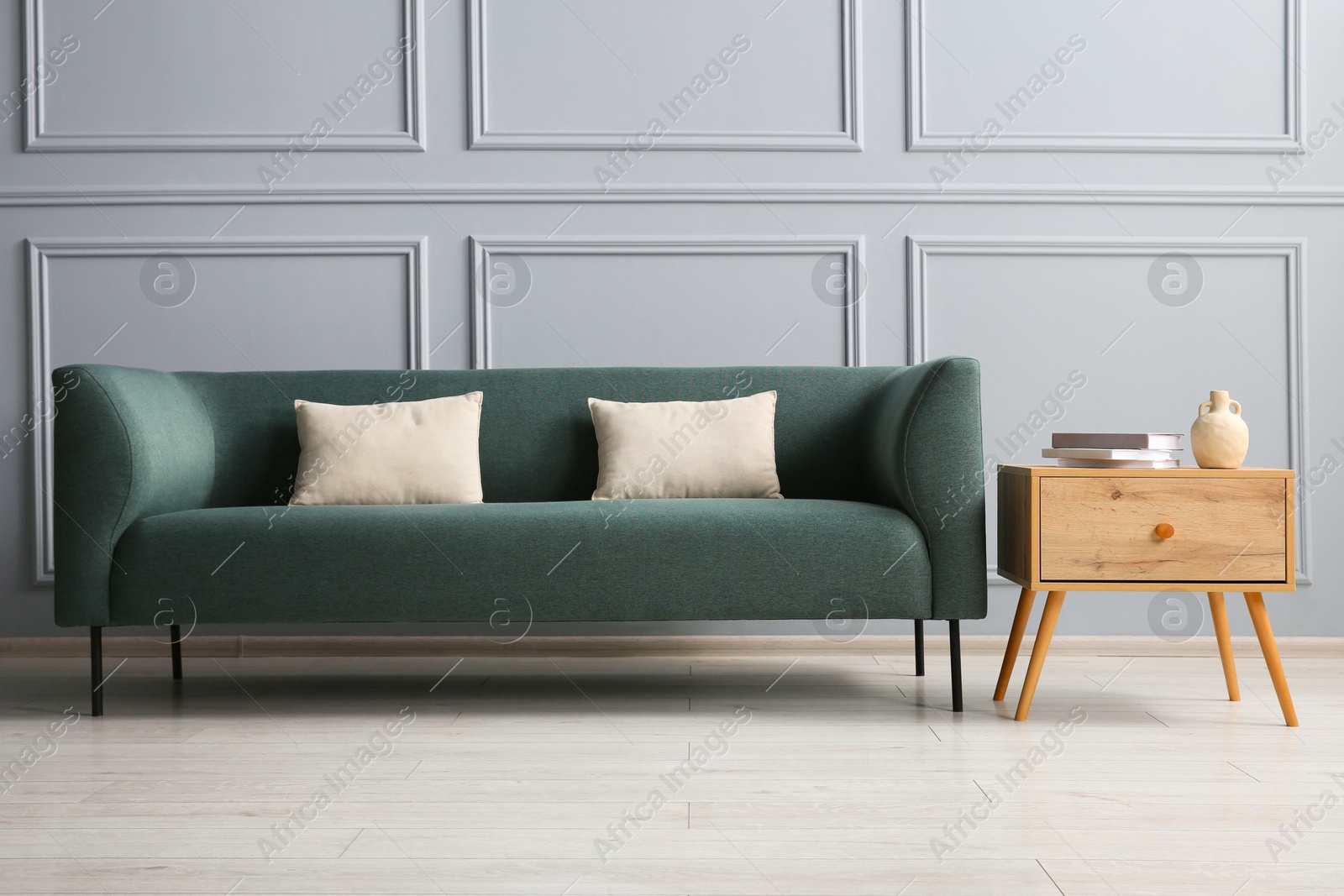 Photo of Stylish sofa with cushions and books on side table near grey wall