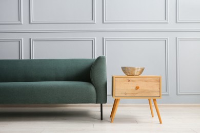 Photo of Stylish sofa and bowl on side table near grey wall