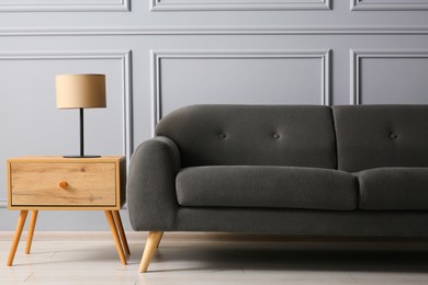 Photo of Stylish sofa and lamp on side table near grey wall