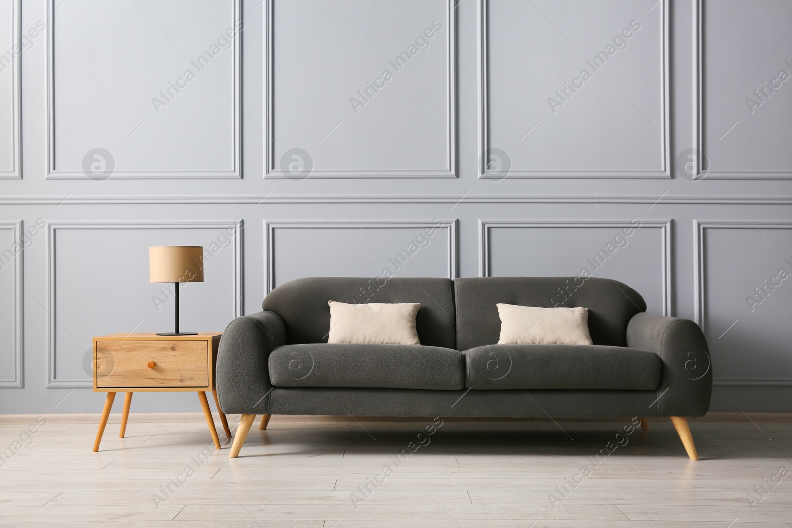 Photo of Stylish sofa with cushions and lamp on side table near grey wall