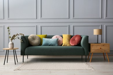 Photo of Stylish sofa with cushions, lamp and eucalyptus branches in vase on side tables in room