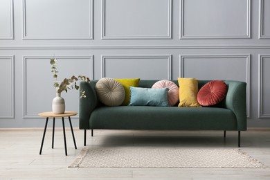 Stylish sofa with cushions and eucalyptus branches in vase on side table near grey wall