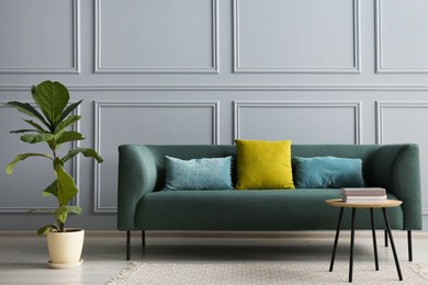 Stylish sofa with cushions, plant and books on coffee table in room