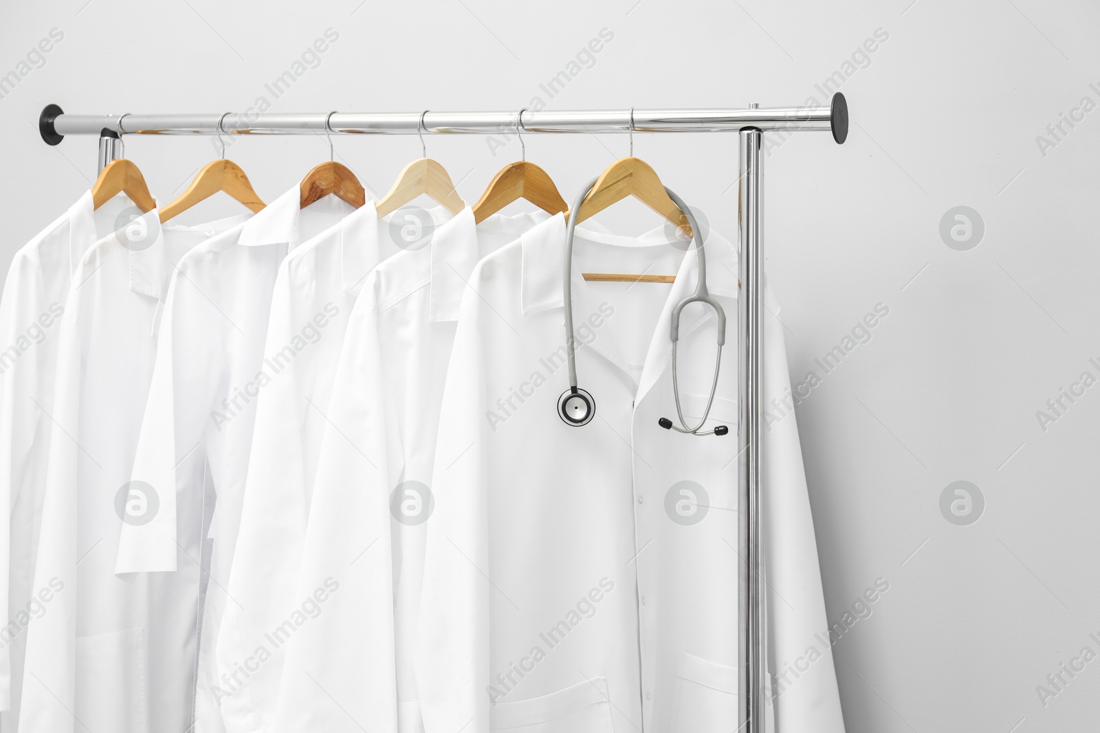 Photo of Different medical workers' uniforms and stethoscope on clothing rack against grey background