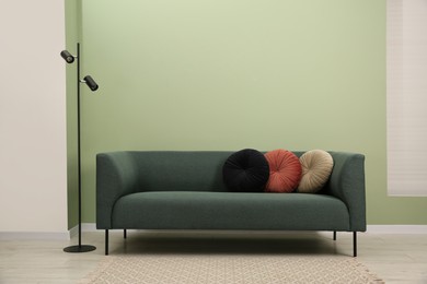 Photo of Stylish sofa with pillows and lamp near green wall indoors