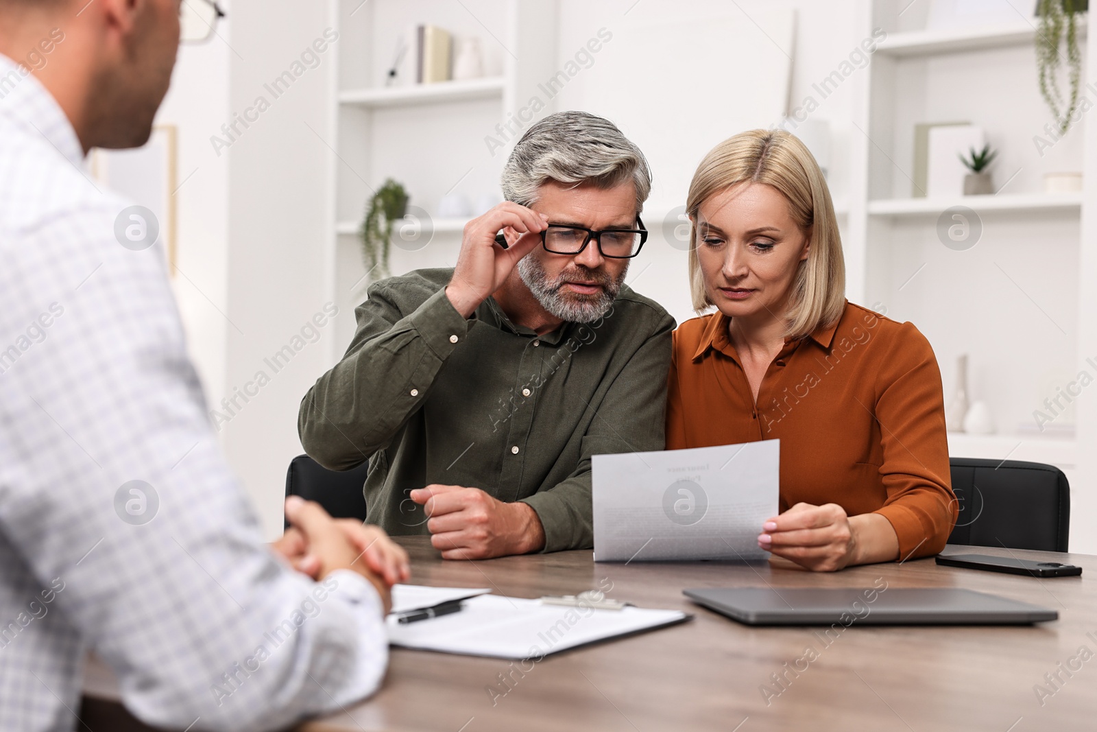 Photo of Pension plan. Couple consulting with insurance agent at table indoors