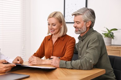 Pension plan. Couple consulting with insurance agent at table indoors