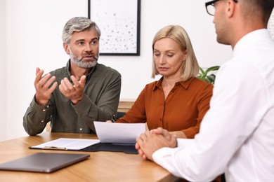 Pension plan. Couple consulting with insurance agent at table indoors