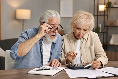 Pension savings. Senior couple planning budget at wooden table indoors