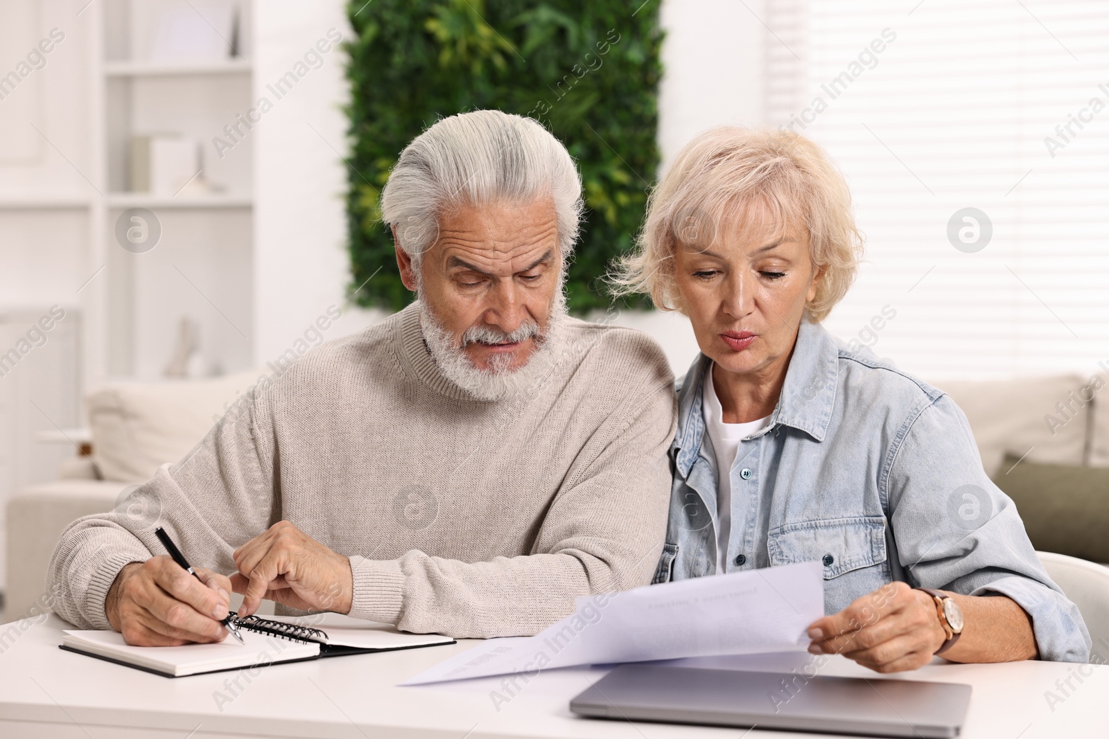 Photo of Pension savings. Senior couple planning budget at white table indoors