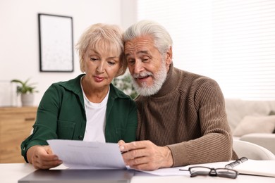 Photo of Pension savings. Senior couple planning budget at white table indoors