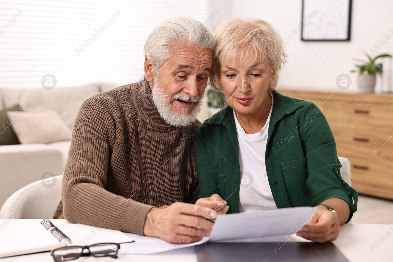 Photo of Pension savings. Senior couple planning budget at white table indoors