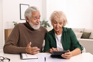 Photo of Pension savings. Senior couple planning budget at white table indoors