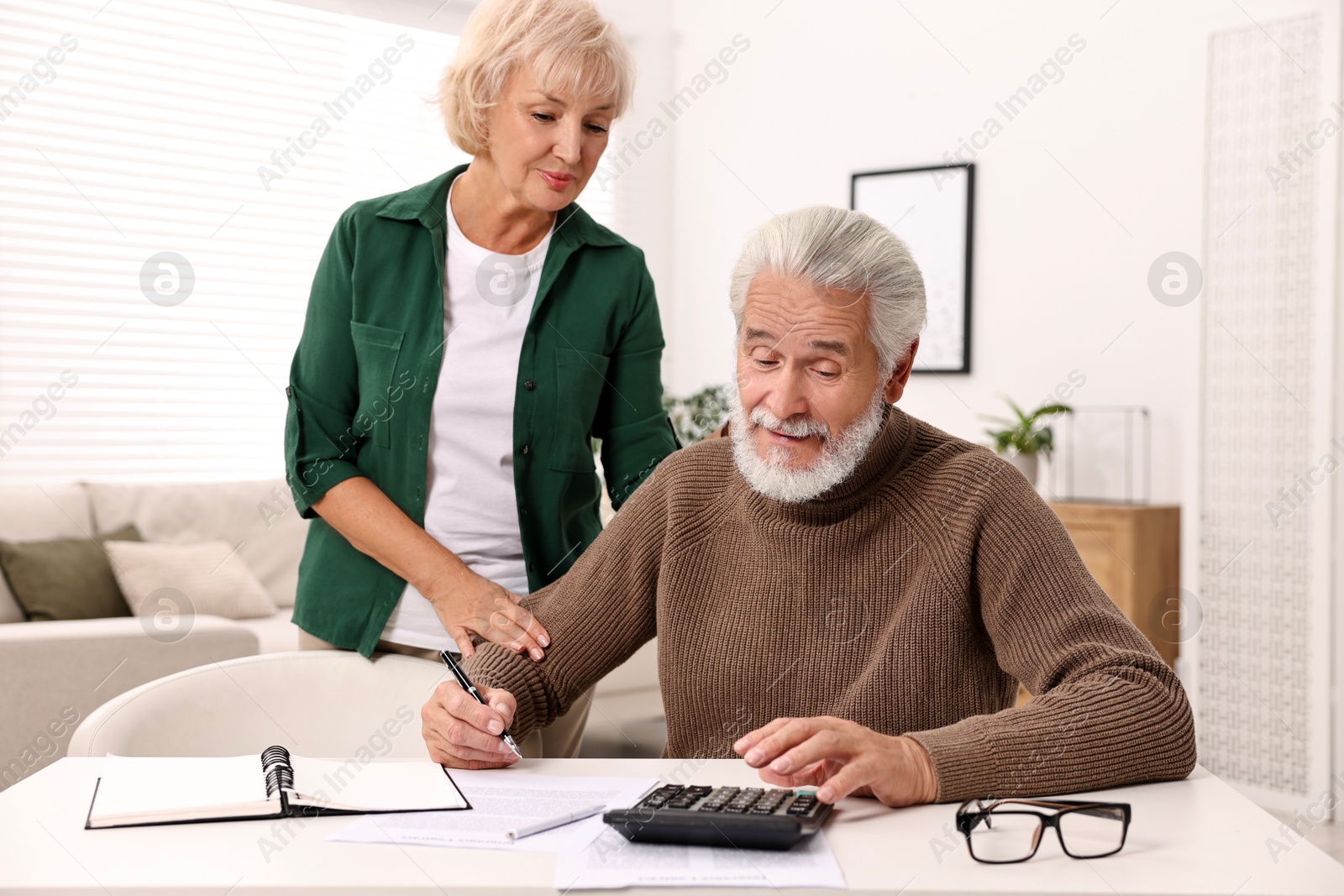 Photo of Pension savings. Senior couple planning budget at white table indoors