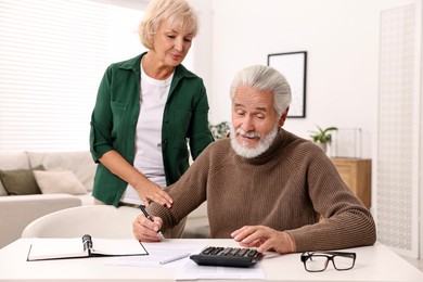 Photo of Pension savings. Senior couple planning budget at white table indoors