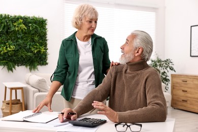 Photo of Pension savings. Senior couple planning budget at white table indoors