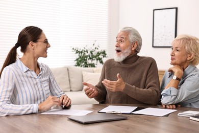 Pension plan. Senior couple consulting with insurance agent at wooden table indoors