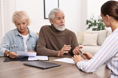 Pension plan. Senior couple consulting with insurance agent at wooden table indoors