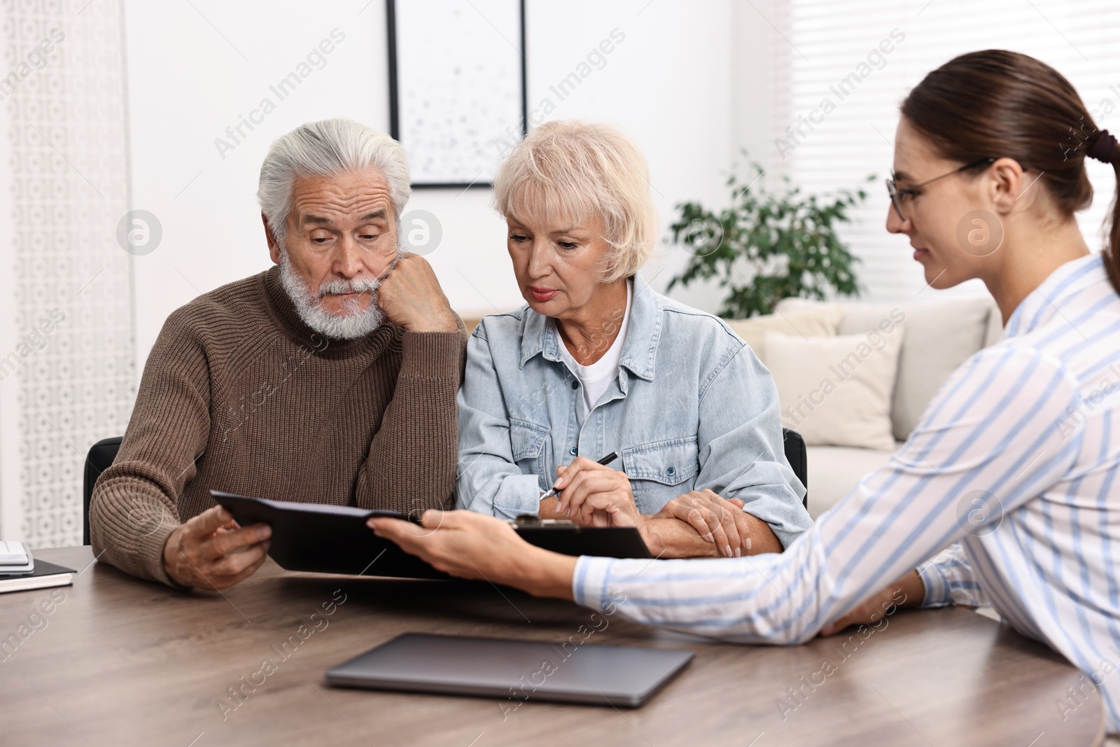 Photo of Pension plan. Senior couple consulting with insurance agent at wooden table indoors