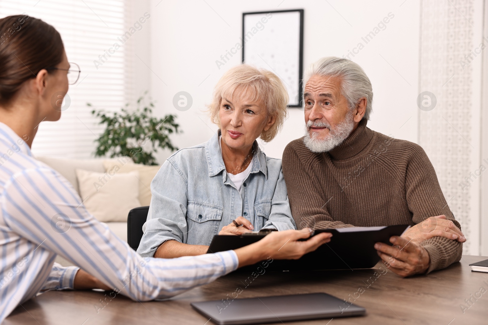 Photo of Pension plan. Senior couple consulting with insurance agent at wooden table indoors