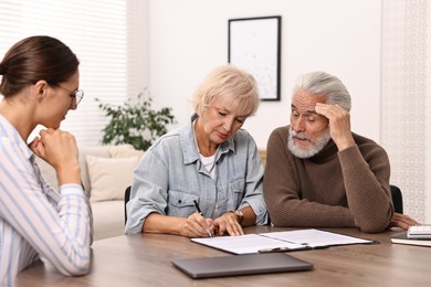 Photo of Pension plan. Senior couple consulting with insurance agent at wooden table indoors