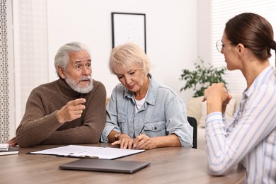 Pension plan. Senior couple consulting with insurance agent at wooden table indoors