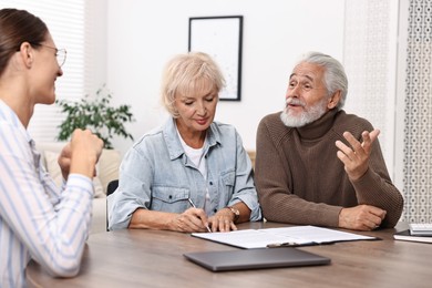 Pension plan. Senior couple consulting with insurance agent at wooden table indoors