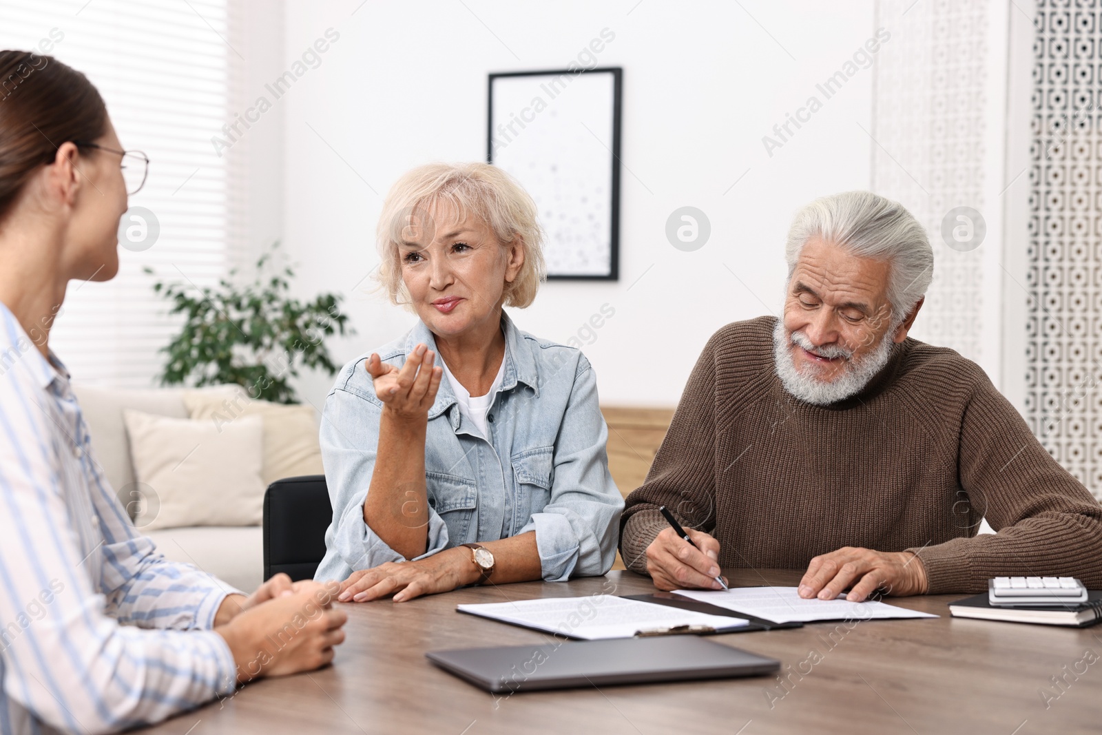 Photo of Pension plan. Senior couple consulting with insurance agent at wooden table indoors